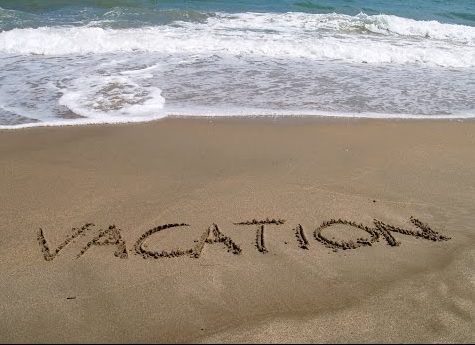 The word "vacation" written in the sand with the shoreline behind it for the blog "How to Avoid a Flood During Vacation"